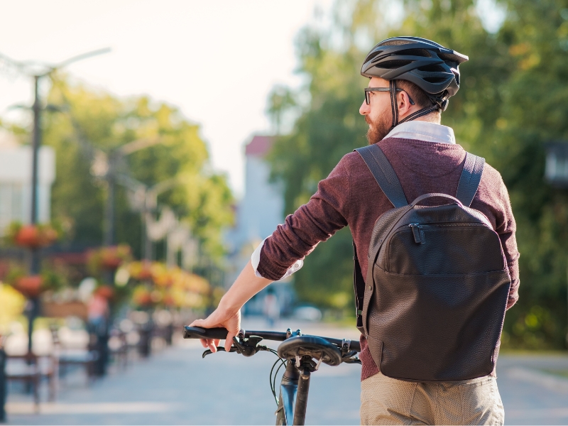 male walking bike wearing a backpack and helmet, face in profile 