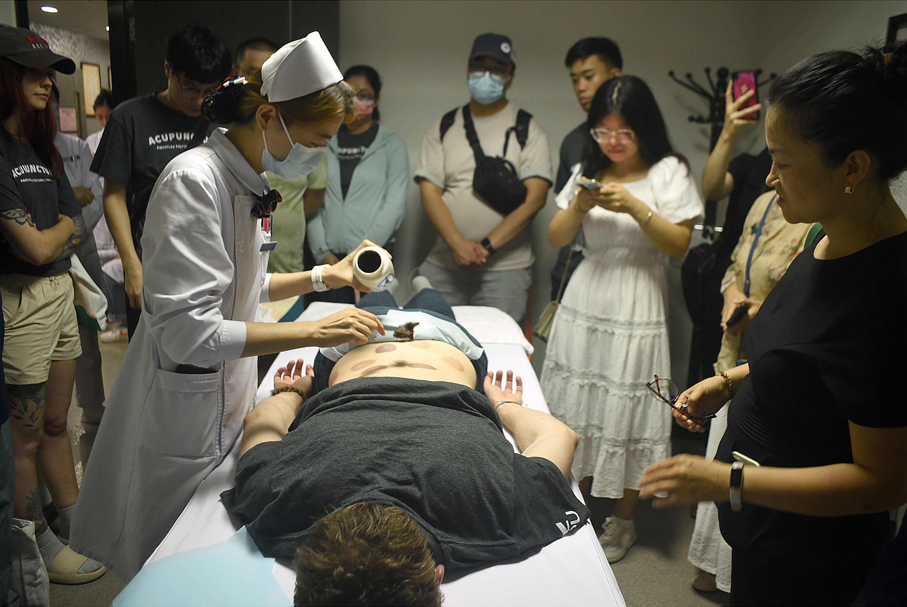 KPU student receiving an application of a herbal paste, followed by a massage with a heated Bian Stone device.