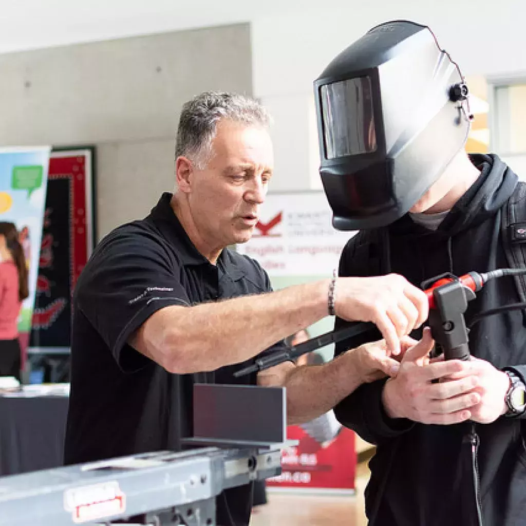 An instructor shows an attendee at a KPU open house how to use the virtual welding machine.