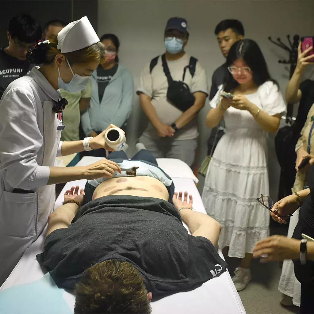 KPU student receiving an application of a herbal paste, followed by a massage with a heated Bian Stone device.