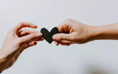 two hands holding a black paper heart