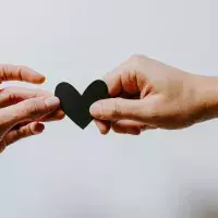 two hands holding a black paper heart